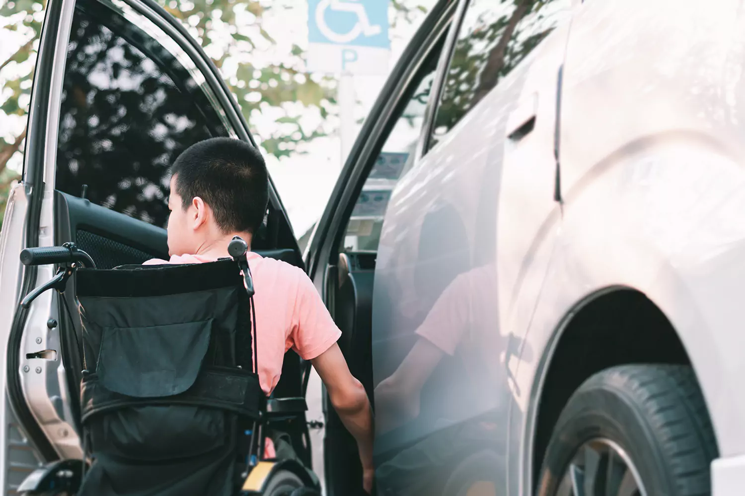 A young disabled man is sitting in a wheelchair waiting to be lifted into the front seat of a car